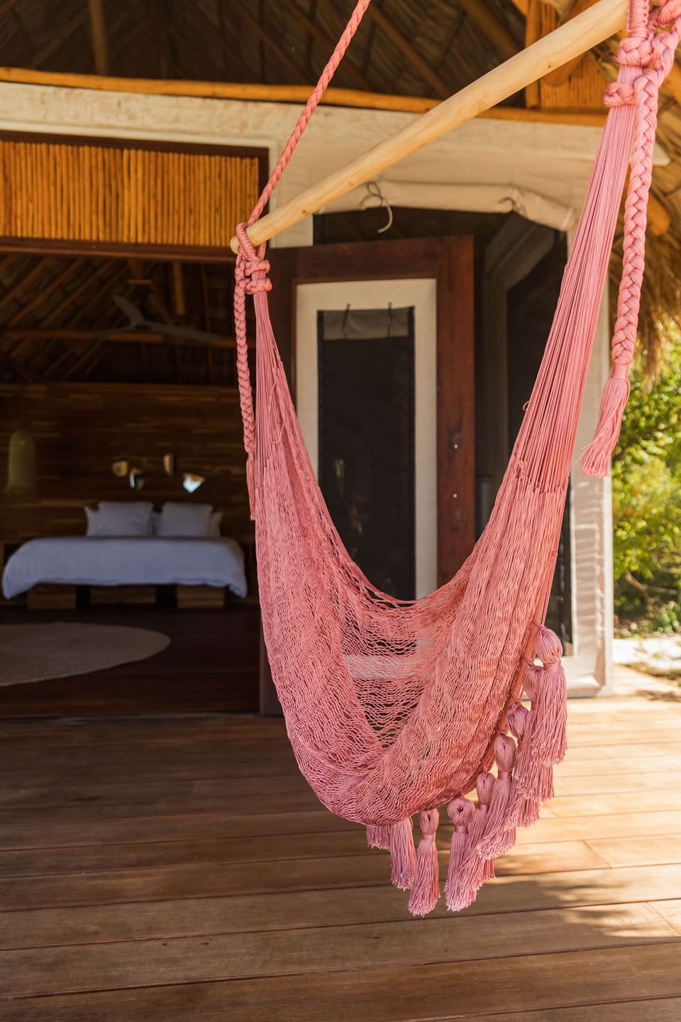 Pink woven hammock hangs from a thatched patio for breezy afternoon naps.