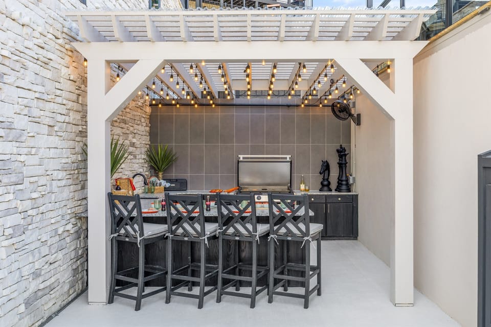 Modern outdoor kitchen and bar with string lights, premium grill, bar seating, and sleek cabinetry. This space is built for outdoor dining and socializing in style and comfort.