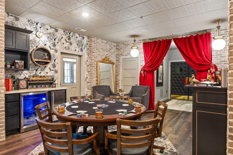 Chic game room with a stylish poker table, vintage-inspired décor, bold red curtains, and a speakeasy vibe. Includes built-in bar and beverage cooler for the ultimate entertaining experience.