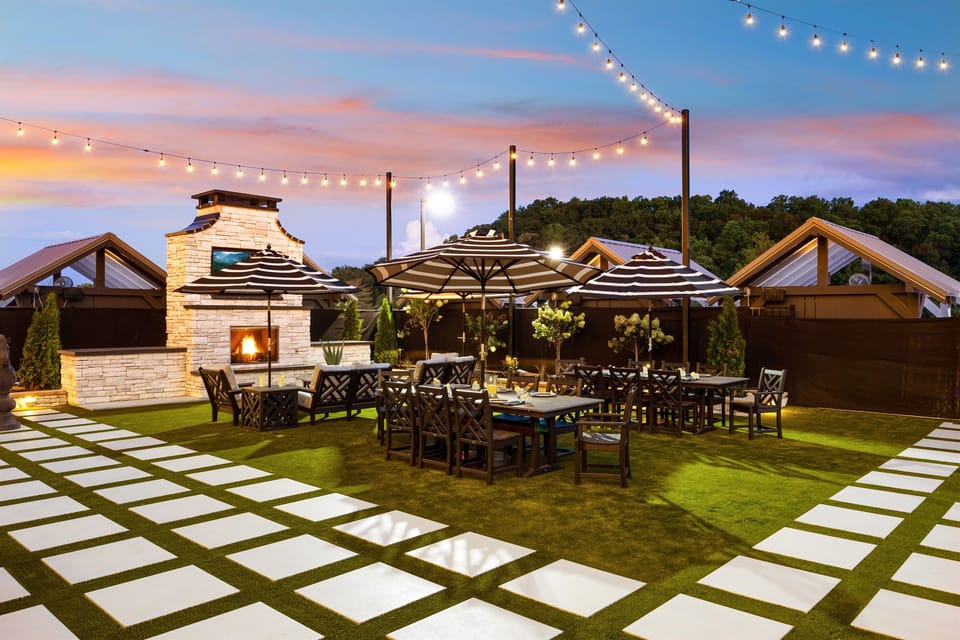 Outdoor dining at its finest—multiple tables, umbrellas, and a beautiful fireplace create the perfect setting for shared meals, celebrations, or casual hangouts under the string-lit sky.