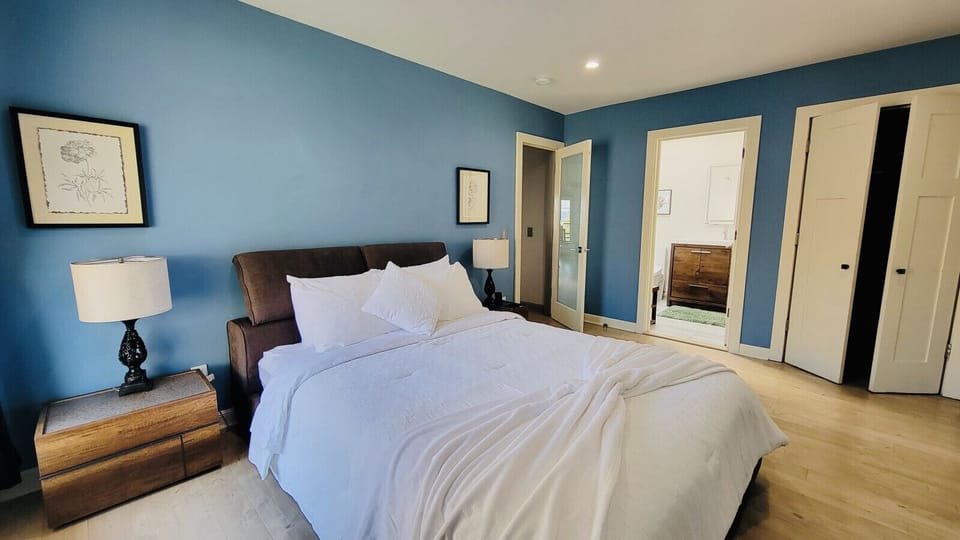 UPSTAIRS:  The master bedroom offers a queen-size bed with crisp white linens, wood-style flooring, and recessed lighting that enhances its modern design.