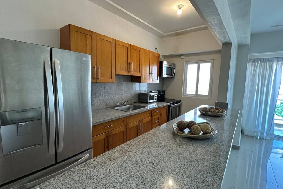 Cocina con acabados modernos+ refrigerador y microondas, incluye el desayunador con acabados lisos y se aprecia el balcón al fondo