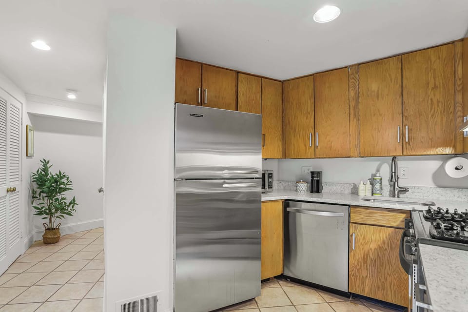 Kitchen with view of the hallway. Kitchen has storage, refrigerator, microwave, dishwasher, coffee maker, oven, stove, soap, and sink. 