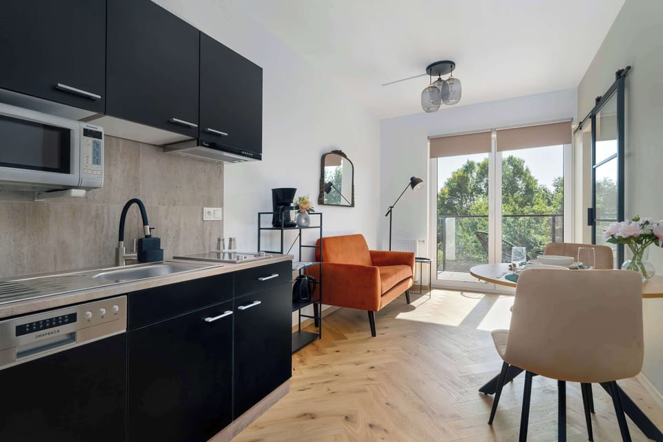 A modern kitchen with dark cabinets and full equipment opens onto a bright living room with access to the balcony.