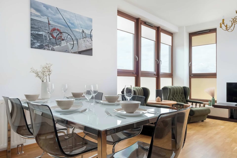 A dining area with a table set for six and modern black chairs. Large windows bring in plenty of light, highlighting the contemporary decor.