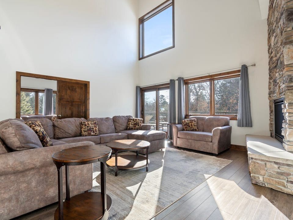Relax in your spacious living room with cozy sectional seating, natural light streaming through large windows, and a beautiful stone fireplace.