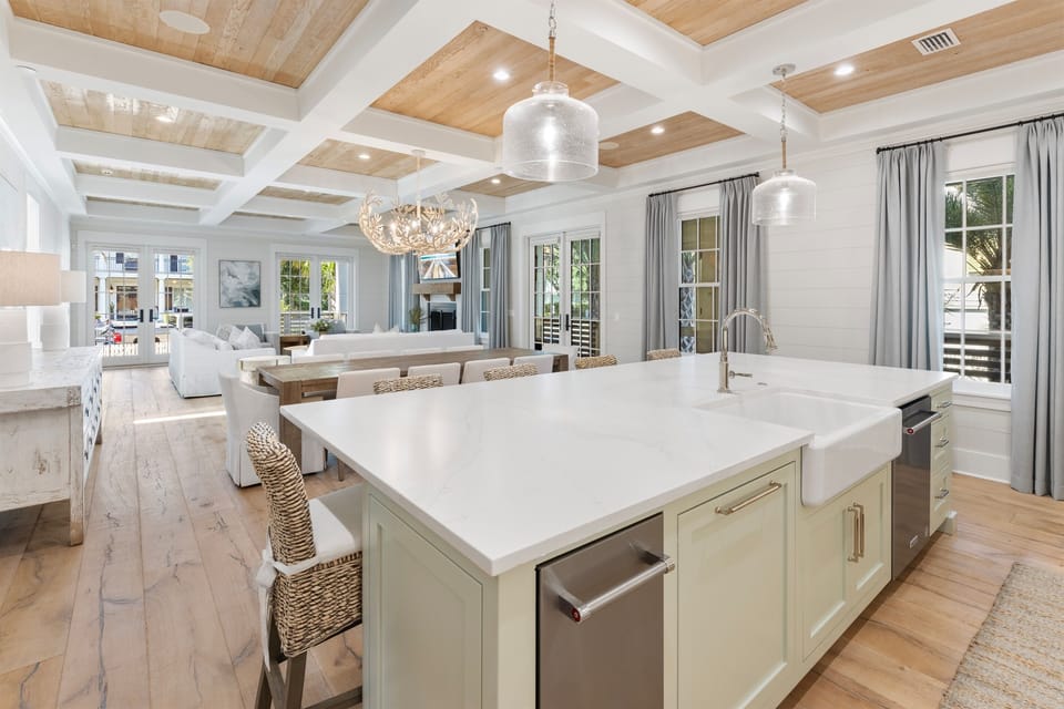 Your gourmet kitchen flows seamlessly into the living space, where natural light pours through elegant windows and coffered ceilings create warmth above.