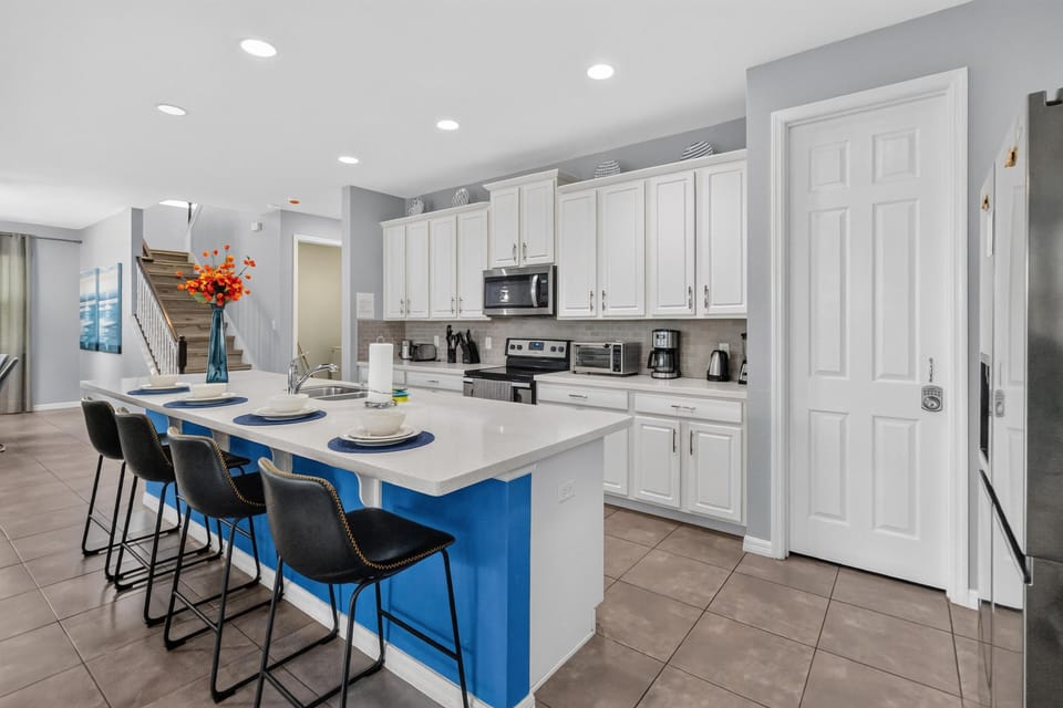 White cabinetry and stainless steel appliances line the kitchen, with a blue island and four black barstools.