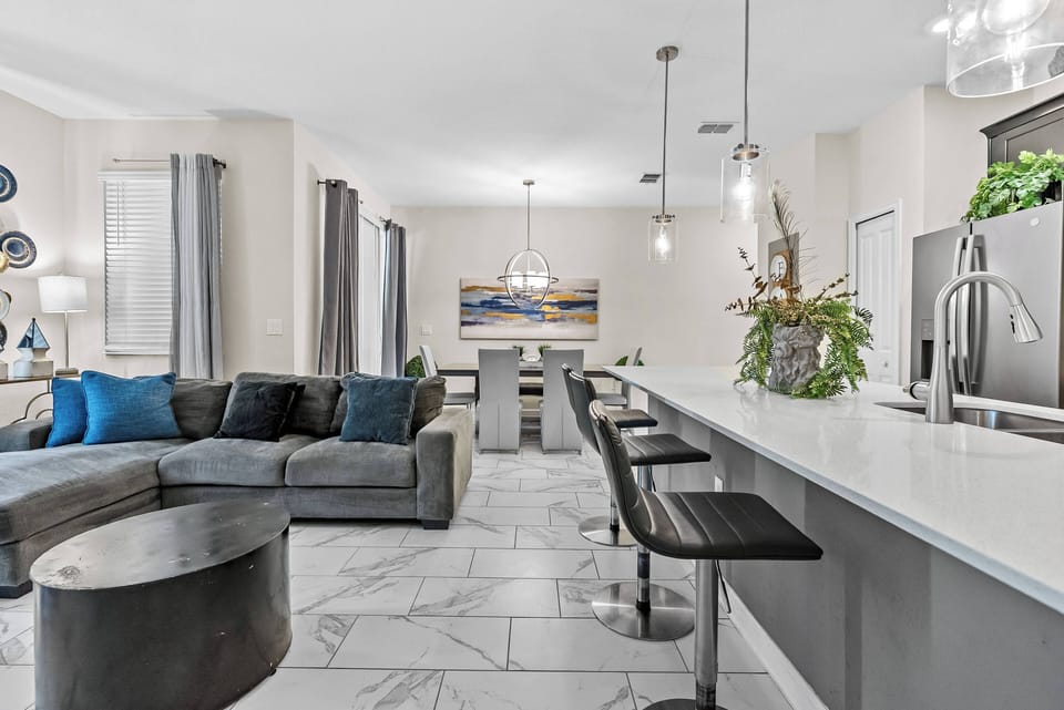 Experience a stylish kitchen and living area bathed in natural light, featuring sleek white countertops and modern bar stools. Unique artwork brings a vibrant touch, creating an inviting atmosphere for your stay.