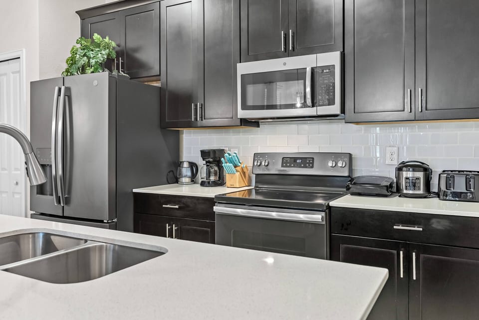 This stylish kitchen boasts sleek black cabinetry and light quartz countertops, complemented by modern stainless steel appliances like a spacious fridge and microwave, making meal prep easy and entertaining a delight.