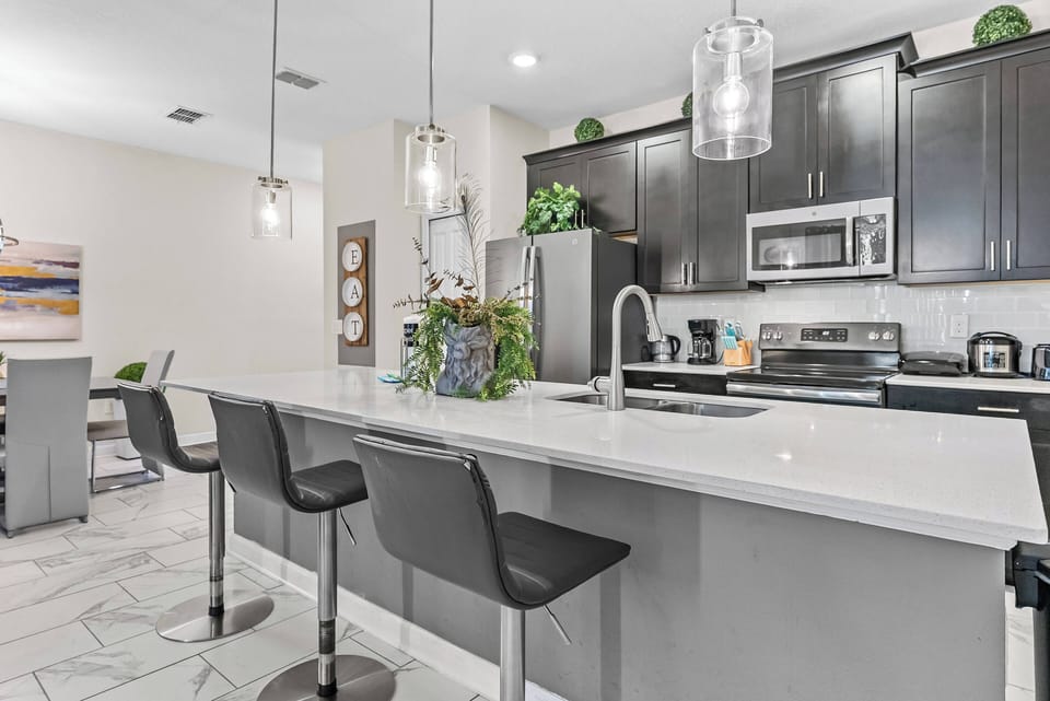 Savor culinary delights in a modern kitchen with sleek black cabinetry and a spacious white countertop. The stylish pendant lighting sets a warm ambiance, while state-of-the-art appliances ensure a convenient and enjoyable stay.
