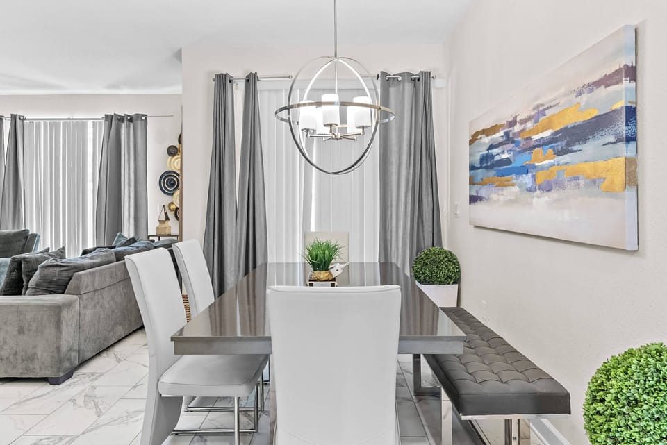 Enjoy your meals in this bright dining area, featuring a sleek glass table and stylish white chairs. A contemporary pendant light adds warmth, while large windows with elegant gray curtains flood the space with natural light.