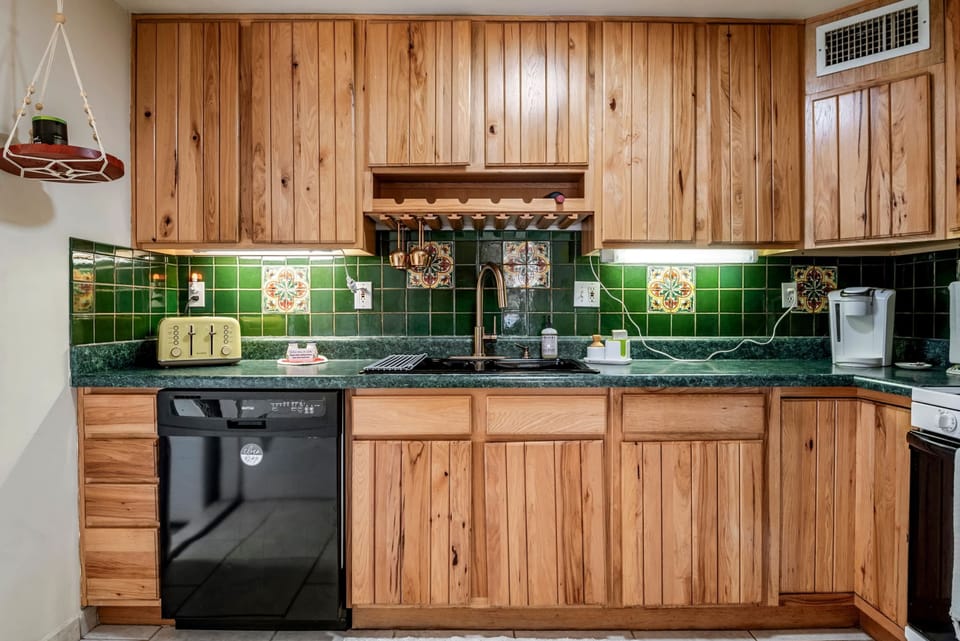 Cook up something delicious in this fully equipped rustic-style kitchen featuring warm wood cabinetry, vibrant green tile backsplash, and whimsical hand-painted accents. Includes essentials like a Keurig coffee maker, toaster, and dishwasher!
