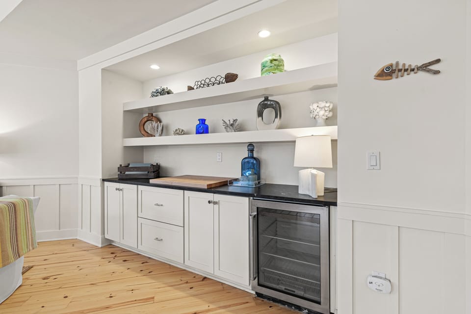 Your private wet bar features elegant built-in shelving, wine fridge, and charming coastal decor for memorable evening entertaining.