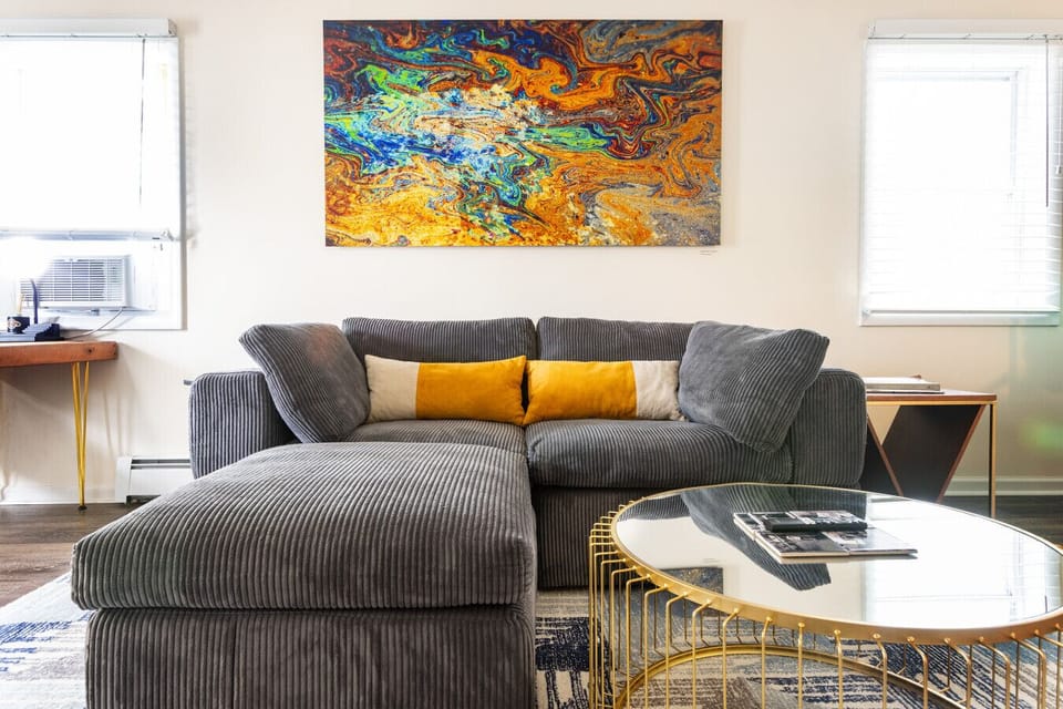 Living room featuring a comfortable couch, a television, and a dining table set over a geometric wool rug. Original modern artwork by Beckerman Photography adds color and creative energy to the vibrant space. 🛋️🎨📺