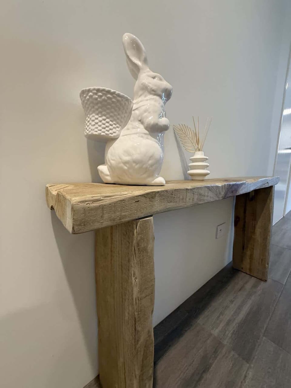 Uniquely handcrafted wood console table. A whimsical porcelain rabbit and a minimalist vase create a blend of rustic charm and modern elegance, offering a warm welcome to your stay.