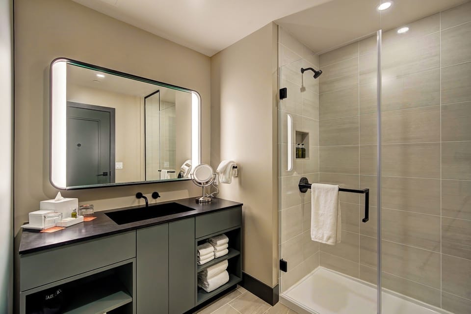 Glass shower with large-format tiles, black countertop, and backlit mirror — a clean reset before the next adventure