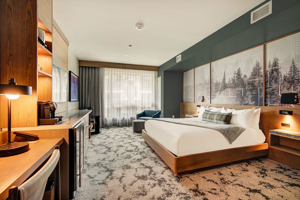 King bed beneath a framed forest mural with desk and accent seating for après-ski evenings