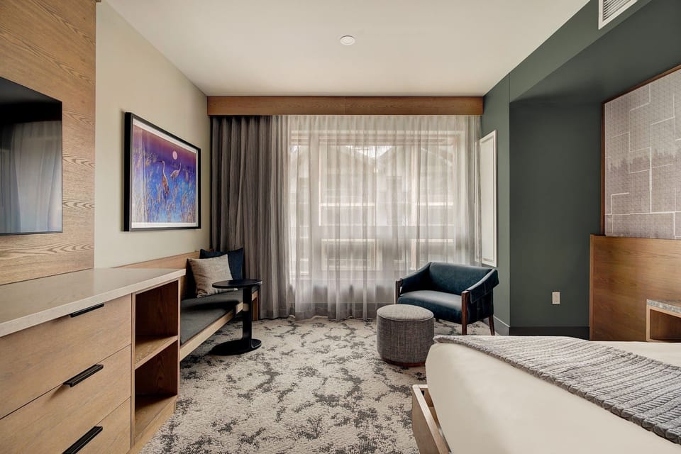 Warm king bed with vibrant wall art, an armchair and ottoman perfect for mountain evenings