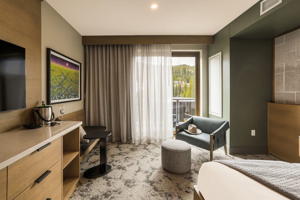 Corner king room with armchair, ottoman, and the balcony door in sight — the view gets better from out there