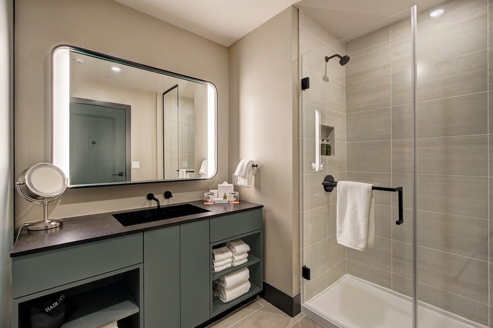 Glass shower and backlit mirror in neutral stone tones — freshen up and get back out to the balcony