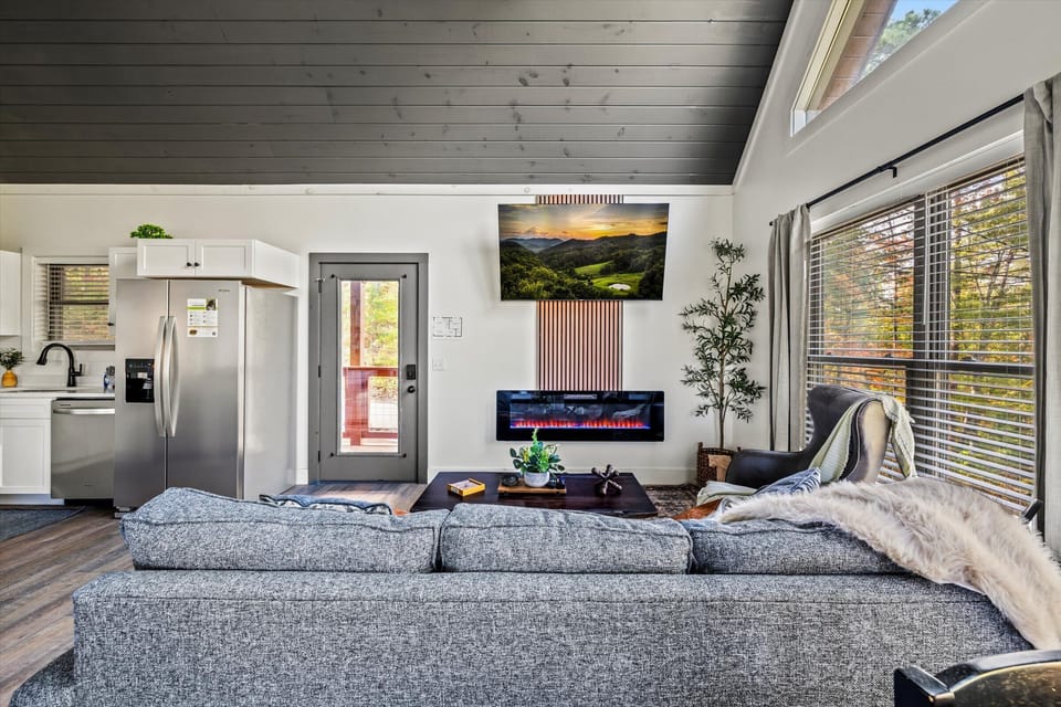 The spacious open-concept living area features a smart TV, electric fireplace, and plenty of room for everyone to relax together. Floor-to-ceiling windows frame stunning mountain views while the queen sleeper sofa provides extra sleeping space.