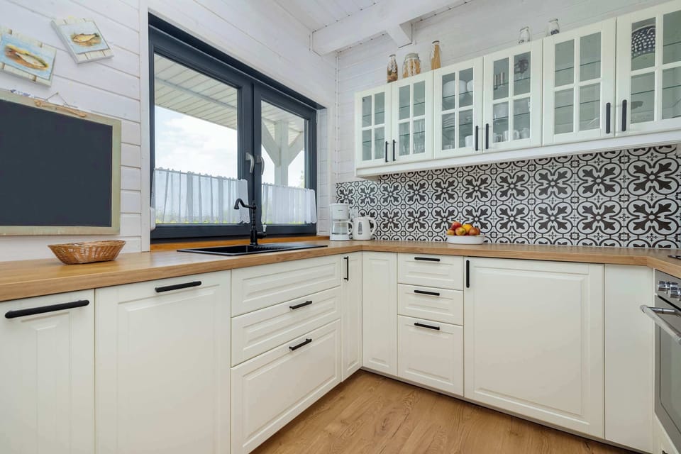 A modern kitchen with cream-colored cabinets, black countertops, and large windows.
