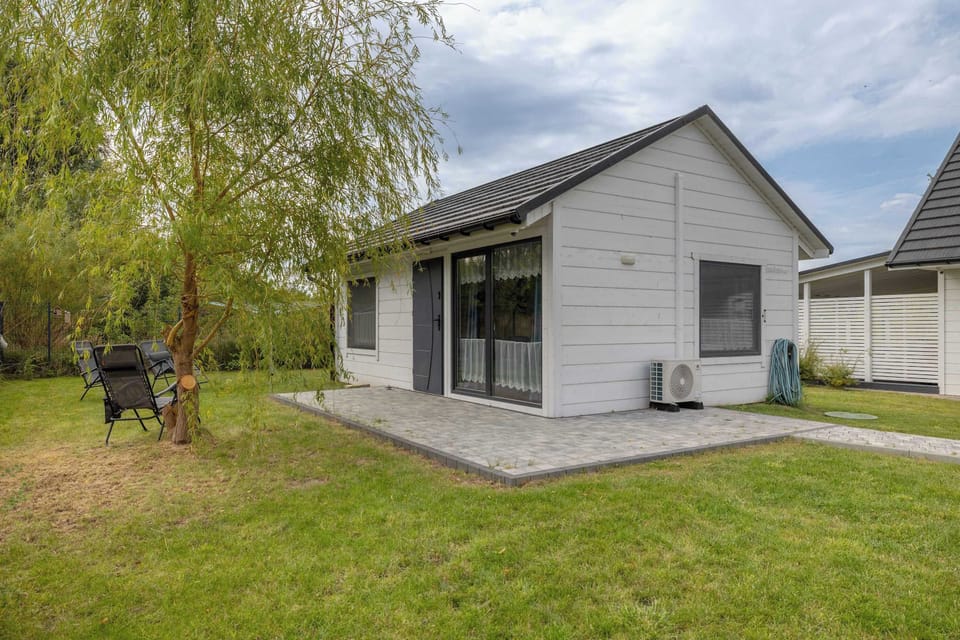 A small garden house painted white with a porch in front. Green grass surrounds the structure.