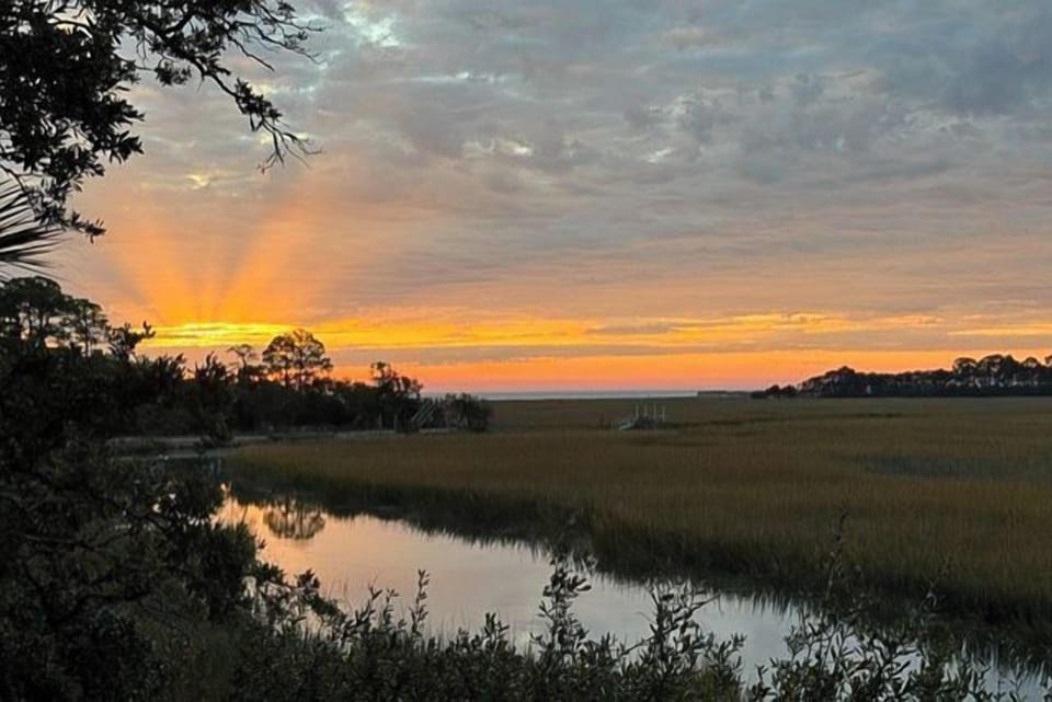 Golden sunset paints the sky over peaceful marshlands, with gentle waters reflecting the warm evening light.