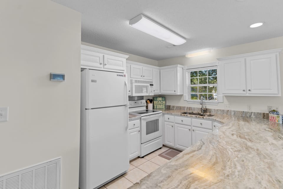 Your fully equipped kitchen awaits with granite countertops, white appliances, and ample cabinet space for preparing memorable vacation meals.