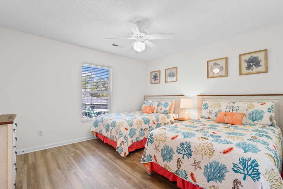 Drift off to sleep in this cheerful coastal-themed bedroom with two beds, ocean-inspired bedding, and gentle ceiling fan keeping you cool.