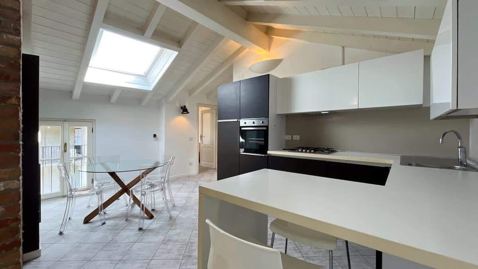 Modern and elegant kitchen, fully equipped with all essential appliances, featuring a peninsula, dining table, skylight, and direct access to the balcony.