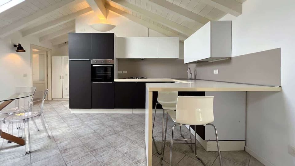 Spacious and bright kitchen with a modern design, equipped with all essential appliances, featuring a large worktop, a convivial peninsula with comfortable seating, and a round glass dining table