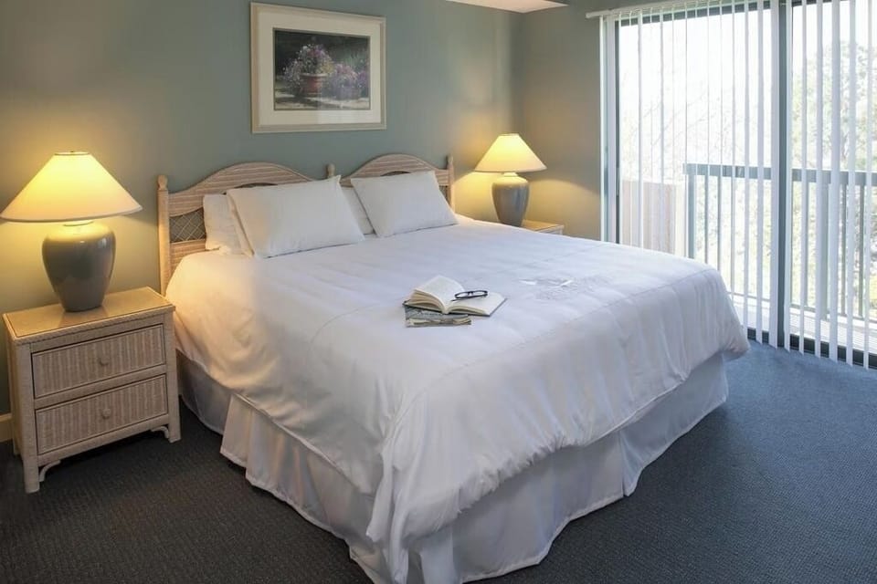 Sink into plush bedding beside sunlit balcony doors.