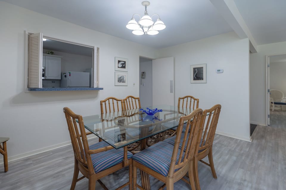 Cozy dining area with a glass-top table, bamboo-style chairs, and coastal-inspired décor, perfect for shared meals and gatherings.