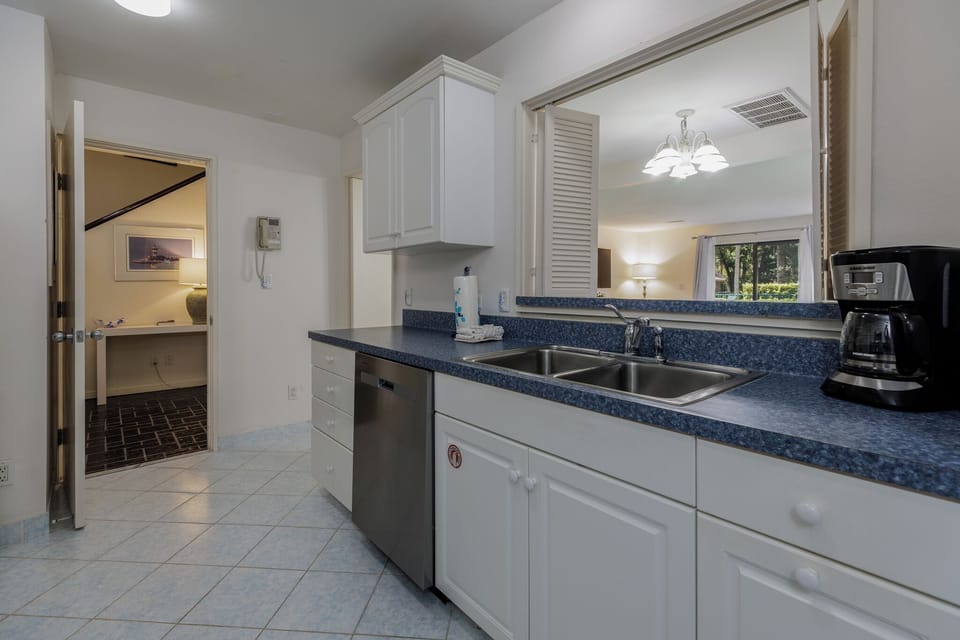Cozy kitchen with ample counter space, double sink, and a pass-through window opening to the bright dining and living area.