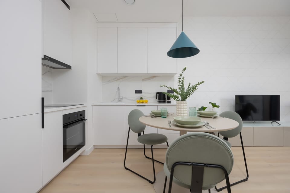 A white modern kitchen with built-in appliances and a round dining table. The design is sleek and functional, perfect for home cooking.