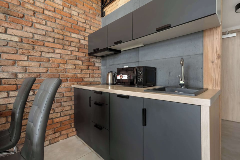 A compact kitchen with black cabinets, wooden shelves, and a coffee machine.