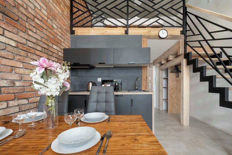 A stylish kitchen area with exposed brick, black cabinets, and a wooden dining table set for four.