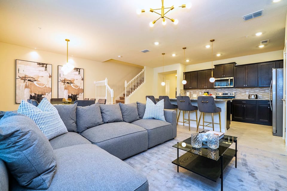 A spacious living area featuring a large family couch and center table with a seamless view of the kitchen island and adjacent dining setup