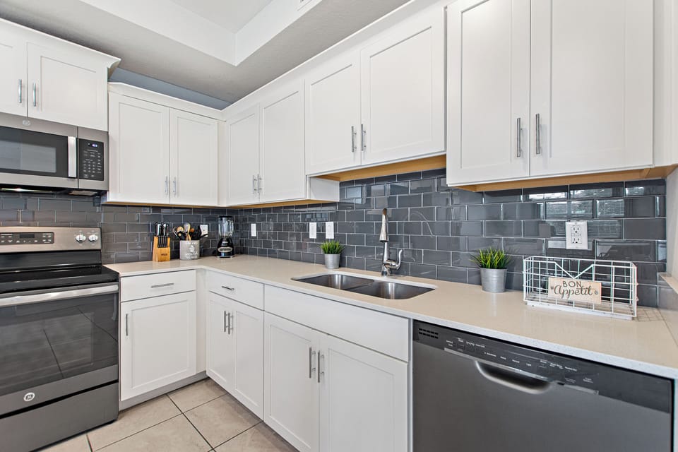 Fully equipped kitchen with white cabinetry, gray tile backsplash and stainless steel appliances – Shine Villas | Sunset Retreat, Storey Lake Resort, Orlando