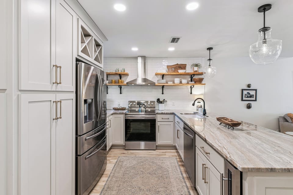 Your chef-worthy kitchen awaits with marble countertops, stainless appliances, and open shelving displaying beautiful dishware.