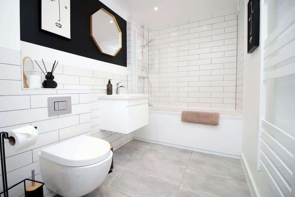Modern, hotel-style bathroom with full bath and overhead rainfall shower. Finished with sleek fittings, fresh white tiling, and plush towels, creating a clean, relaxing space perfect for unwinding after a day out.