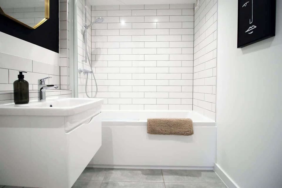 Modern, hotel-style bathroom with full bath and overhead rainfall shower. Finished with sleek fittings, fresh white tiling, and plush towels, creating a clean, relaxing space perfect for unwinding after a day out.