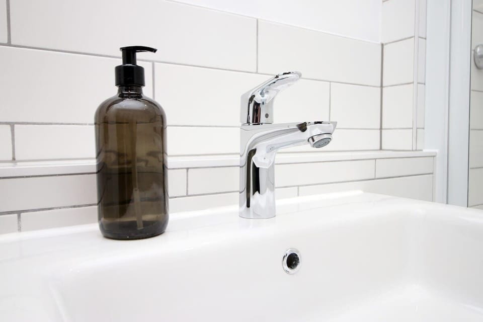 Modern, hotel-style bathroom with full bath and overhead rainfall shower. Finished with sleek fittings, fresh white tiling, and plush towels, creating a clean, relaxing space perfect for unwinding after a day out.