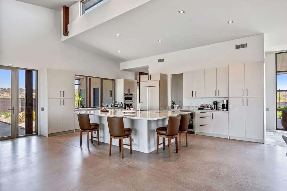 Fully equipped luxury kitchen stocked with all culinary essentials and features high-end stainless-steel appliances, a kitchen island, a dining table, and a wet bar/coffee station.