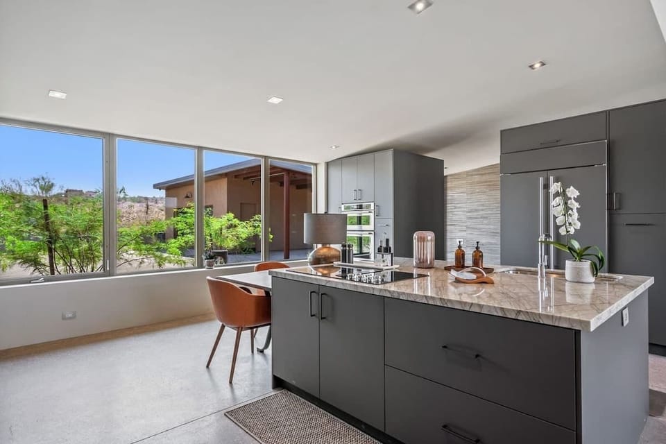 Fully equipped luxury kitchen stocked with all culinary essentials and features high-end stainless-steel appliances, a kitchen island, a breakfast table, and a wet bar / coffee station.