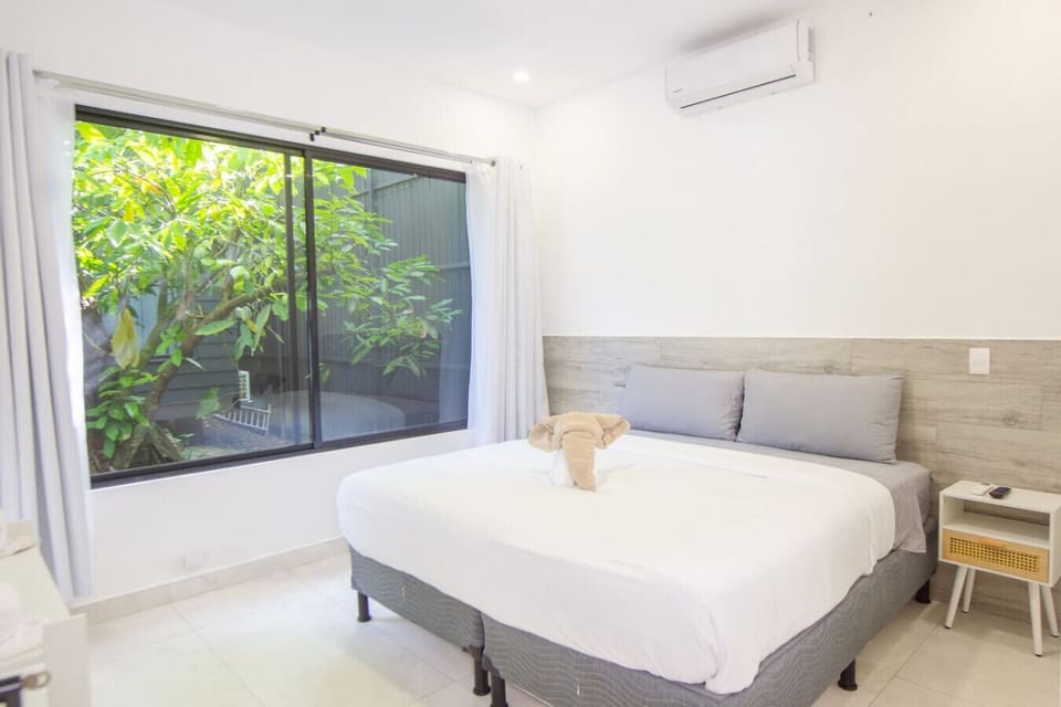 Spacious master bedroom with king-size bed, A/C, and large window showcasing lush tropical garden views, Somnara Villas 4, Playa Chiquita, Costa Rica.
