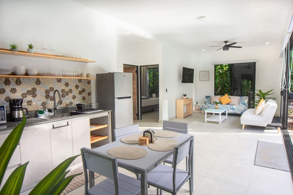 Open-plan living, dining, and kitchen area with modern furnishings, natural light, and garden views, Somnara Villas 4, Playa Chiquita, Costa Rica.
