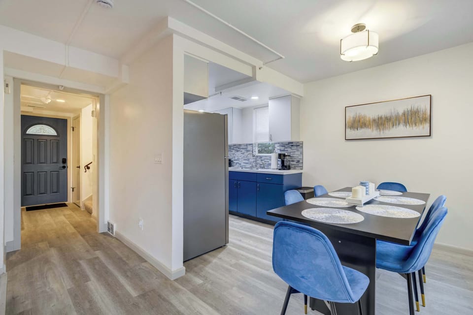 A bright dining space with modern blue chairs and a sleek table, perfect for family meals or game nights, with large windows framing views of the backyard and pergola.